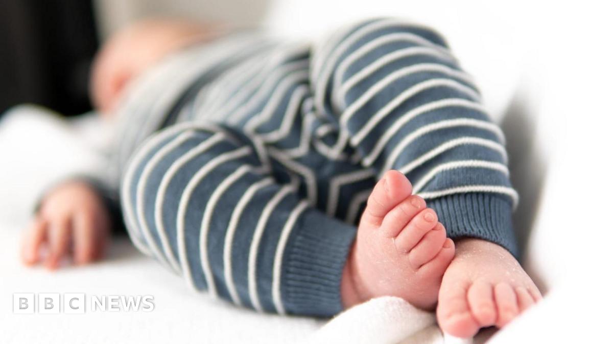 A newborn baby is lying in white sheets, its face is out of focus in the distance, its feet are close to the camera.
