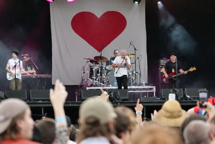 A man singing into a microphone on a stage in the background, with waving hands in the foreground.