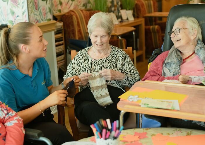 Supportive staff and elderly women knitting in dementia care center