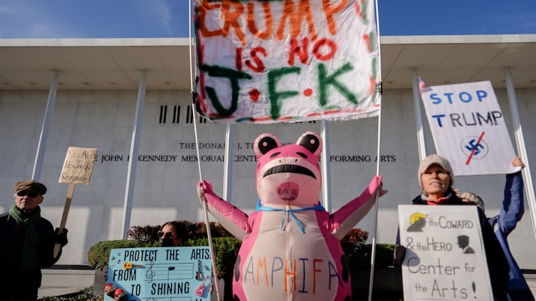 Demonstrators, including Nadine Siler, of Waldorf, Md., dressed in a pink frog costume, hold up signs at a designated protest point in front of the John F. Kennedy Memorial Center for the Performing Arts