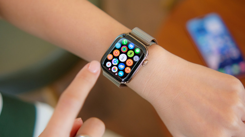 An Apple Watch open to the app menu, the device is on a user's left wrist and their right hand is readying to tap an icon on the screen