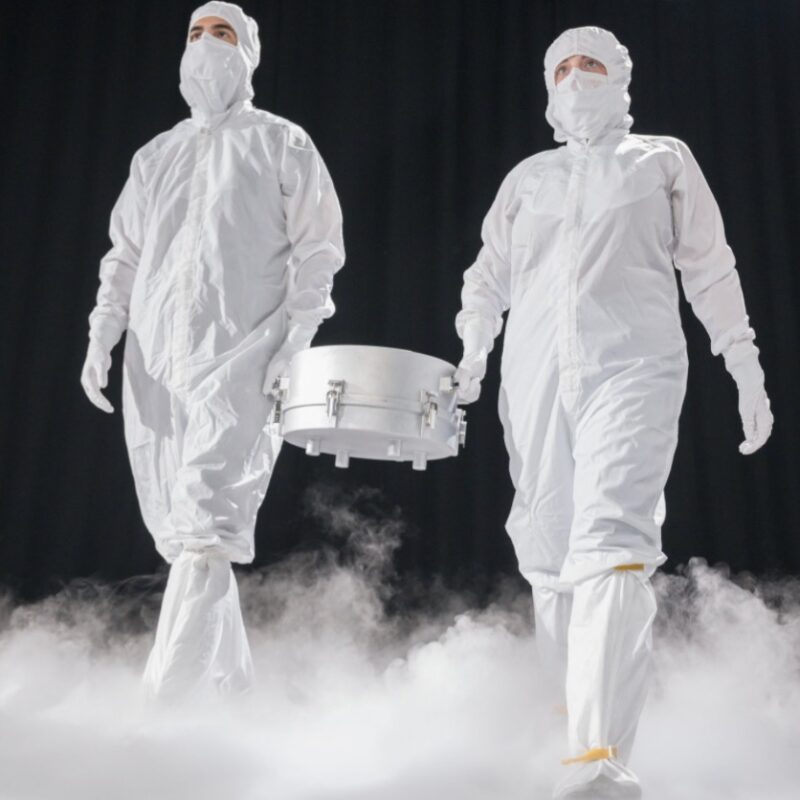 Lunar quarantine facility: Two men in white suits carrying a silver canister between them, in a dark area with white mist boiling up from the floor.