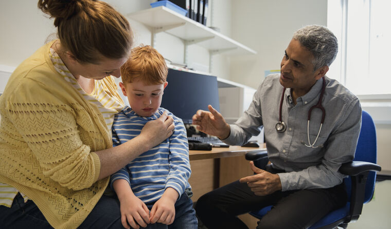 Shy boy sits on mum's lap in male doctor's surgery
