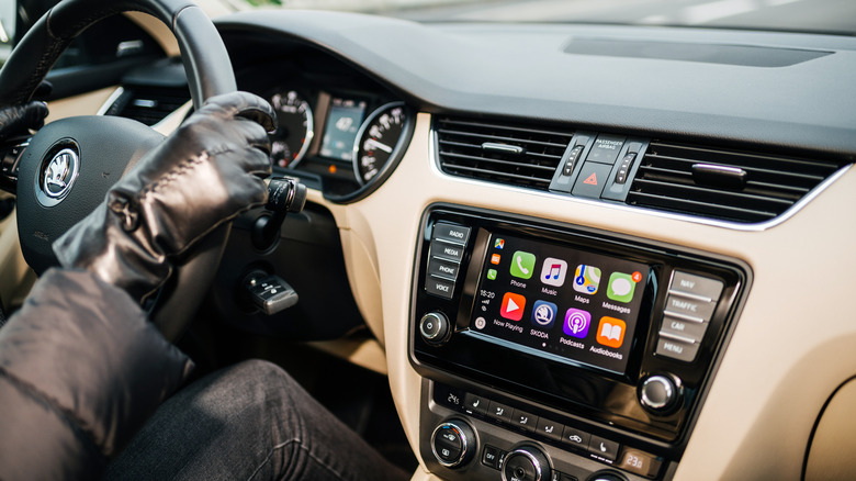 Woman driving Skoda Octavia Czech car wearing leather gloves with large dashboard display computer featuring CarPlay from Apple Computer