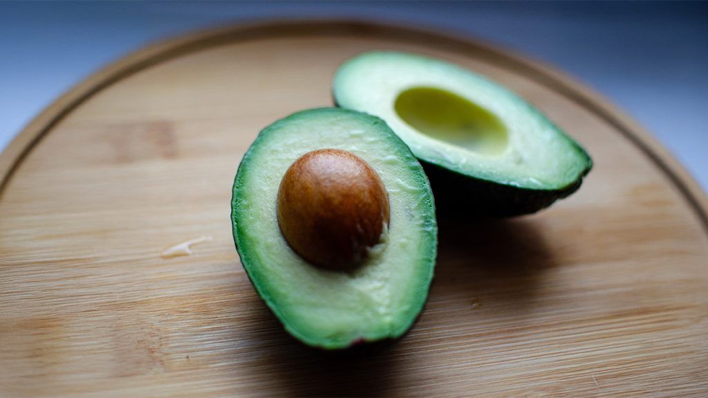 two avocado halves on a wooden chopping board