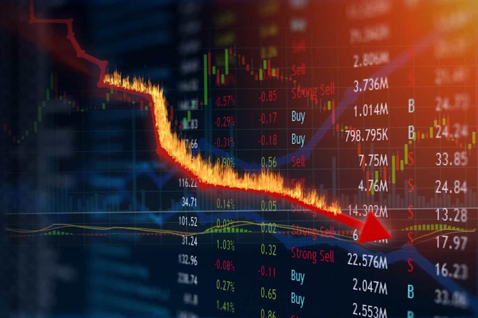 A digital stock market chart with a dark background displays a steep decline. A thick, vibrant red line, engulfed in orange and yellow flames, slopes dramatically downward, ending in a red arrow pointing to the lower right. Green and red candlestick bars are visible in the background, along with numerous financial figures, percentages, and labels like 'Sell' and 'Buy' scattered across the screen.