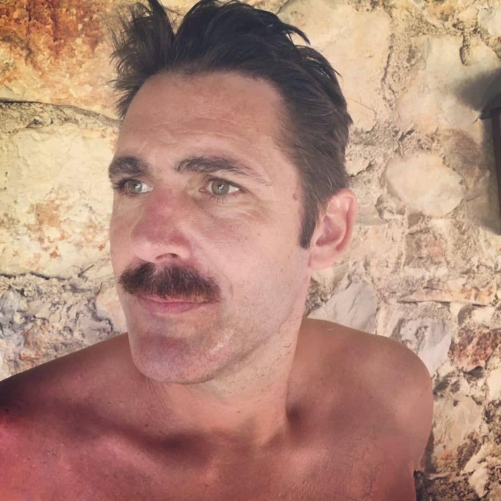 Paul Flack with a moustache in front of a stone wall
