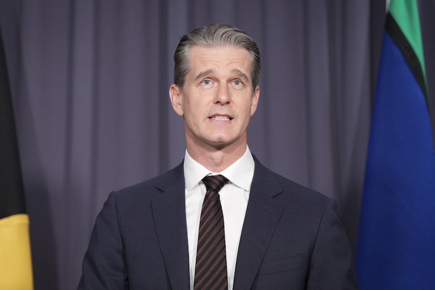 Man in suit and tie stands in front of grey backdrop