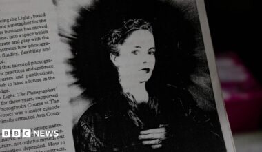 A black and white image of photographer Rhonda Wilson featured in a magazine, with some text to the left of the image. She is wearing a dark jacket and has short hair.