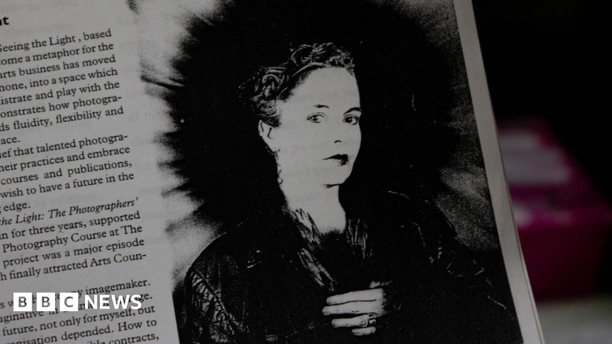A black and white image of photographer Rhonda Wilson featured in a magazine, with some text to the left of the image. She is wearing a dark jacket and has short hair.