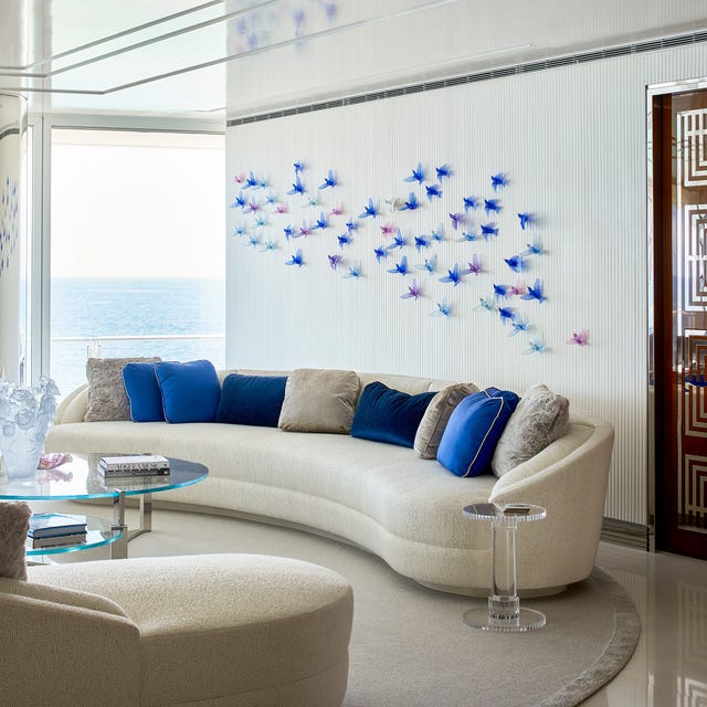 Elegant living room with curved sofa, colorful pillows, glass coffee table, and butterfly wall art.