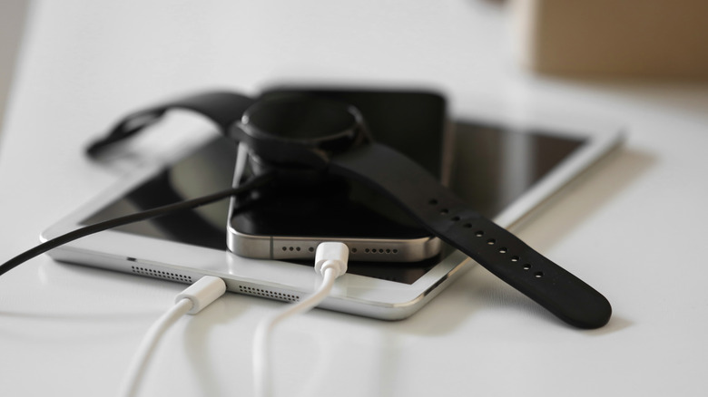 A smartwatch charging on top of a bunch of other charging devices