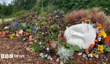 A reclining 'living sculpture', a female cast face with a floral headband and a body covered in flowers