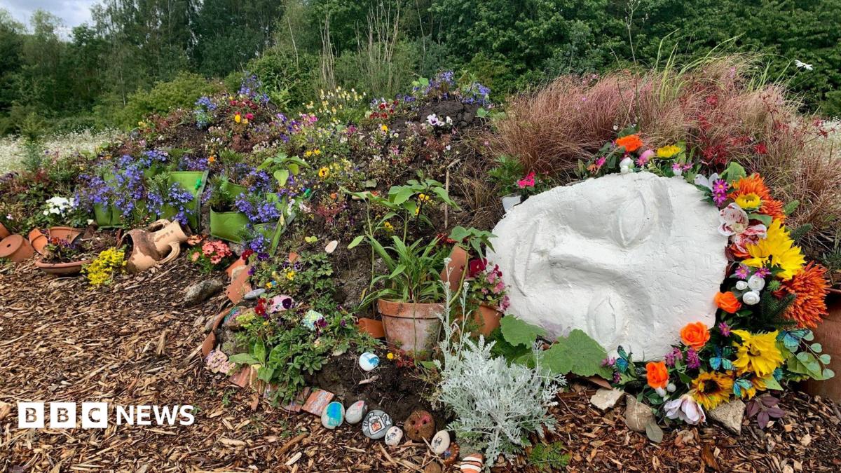 A reclining 'living sculpture', a female cast face with a floral headband and a body covered in flowers