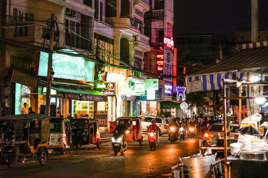 Asian city street at night with lights and motorbikes.