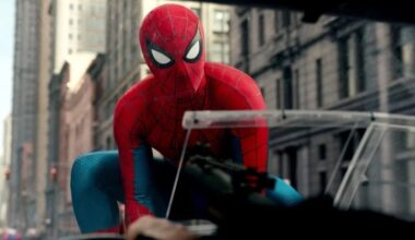 SPider Man in full costume holding onto hood of moving car using webbing