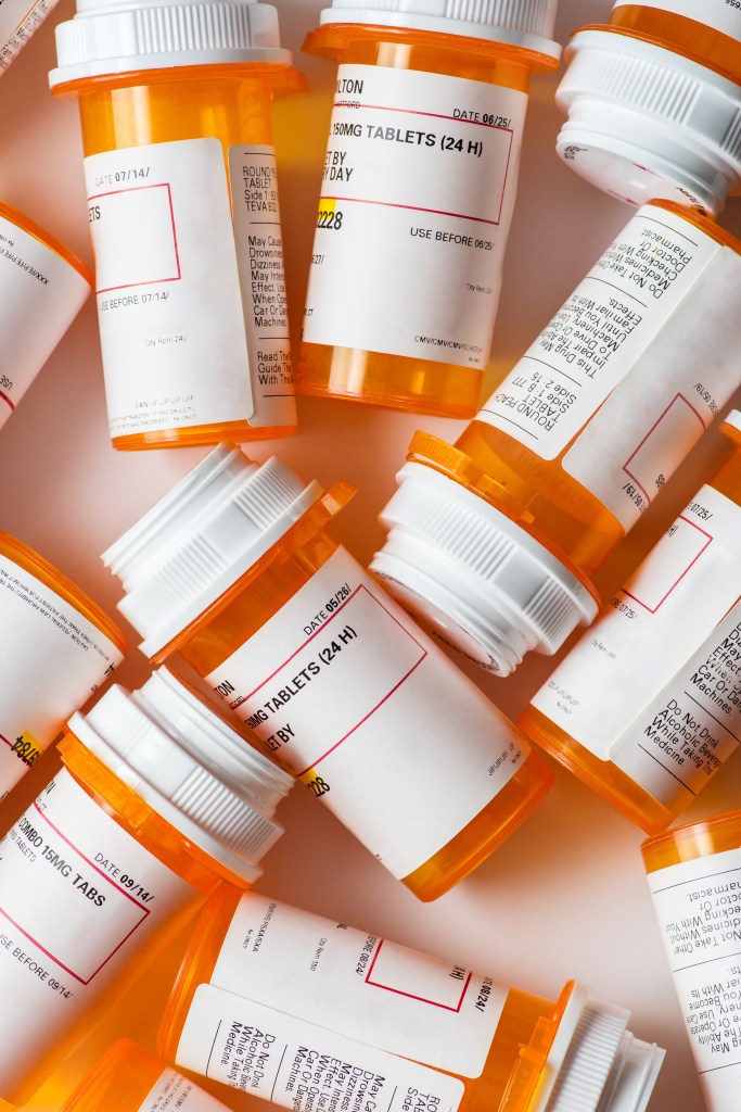 A group of prescription pill bottles with visible labels and warnings scattered on a white background.