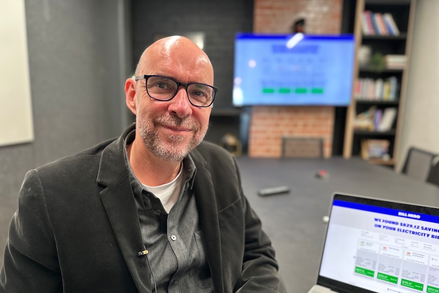 A bespectacled man with a shaved head sits at a computer.