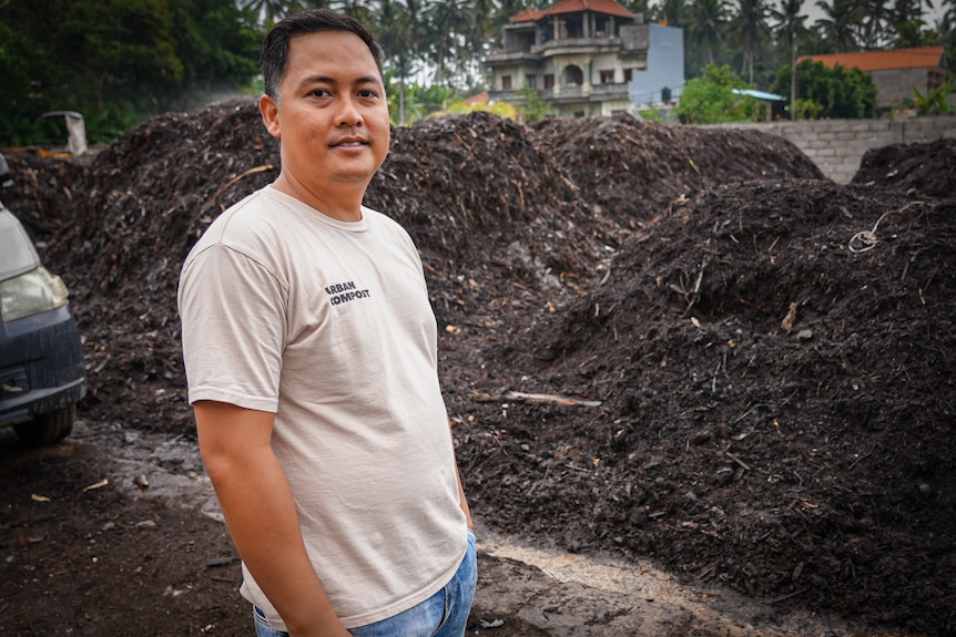 An Indonesian man wearing a white shirt near a mound of dirt.