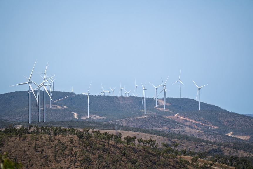 A group of wind turbines dotted along a hillside against a hazy blue sky