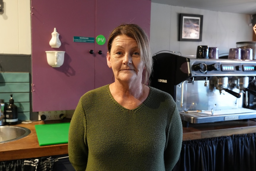 A woman in a cafe stands behind the counter near her coffee machine.