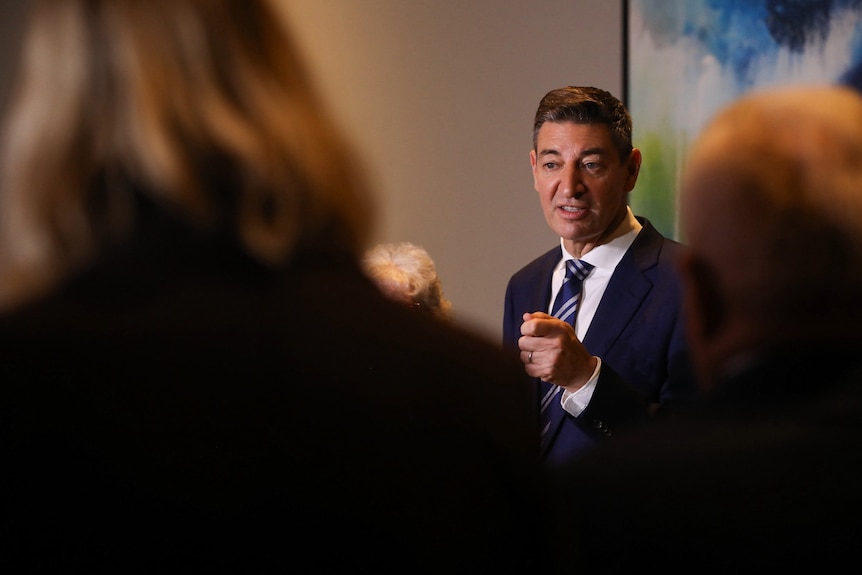 A man in a suit gestures as he speaks to reporters