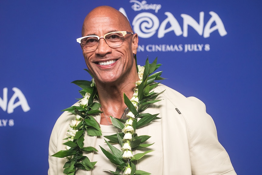 Dwayne Johnson wearing glasses and a wreath around his neck