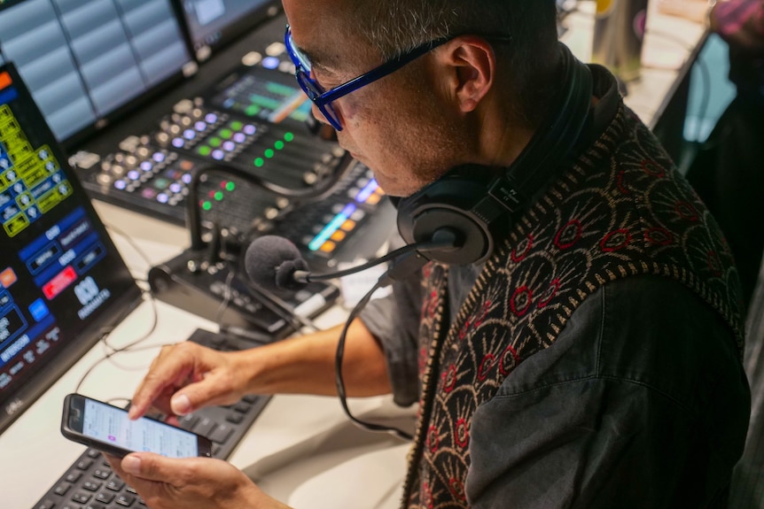 a man looks at his mobile phone while standing at a radio production desk