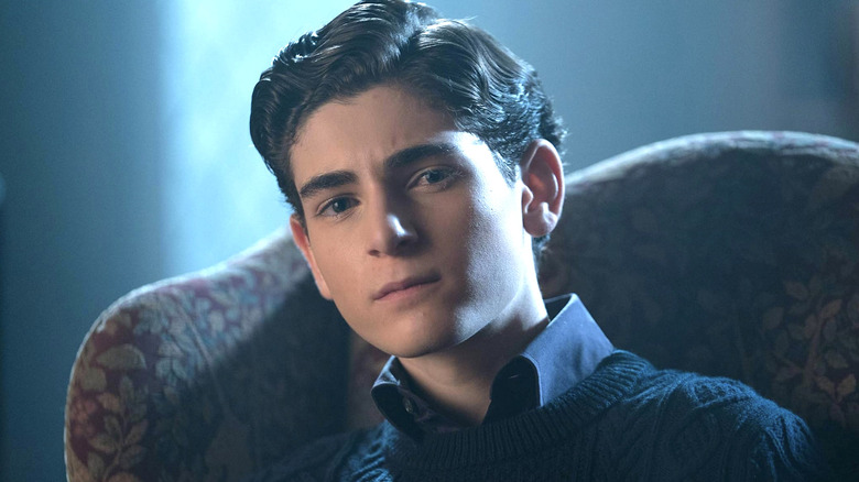 Bruce Wayne sitting in a chair in the dark, wearing a sweater in 
