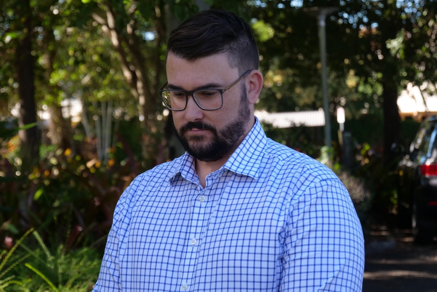 A man wearing glasses stares down at the ground deep in thought.