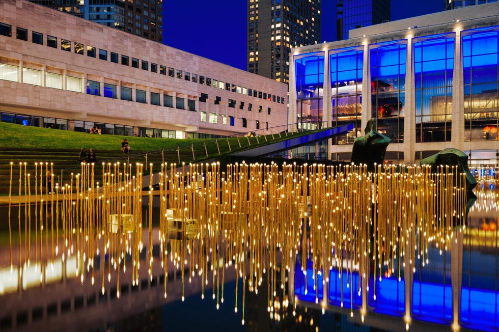 Night scene with glowing lights and modern buildings, reflecting in water.