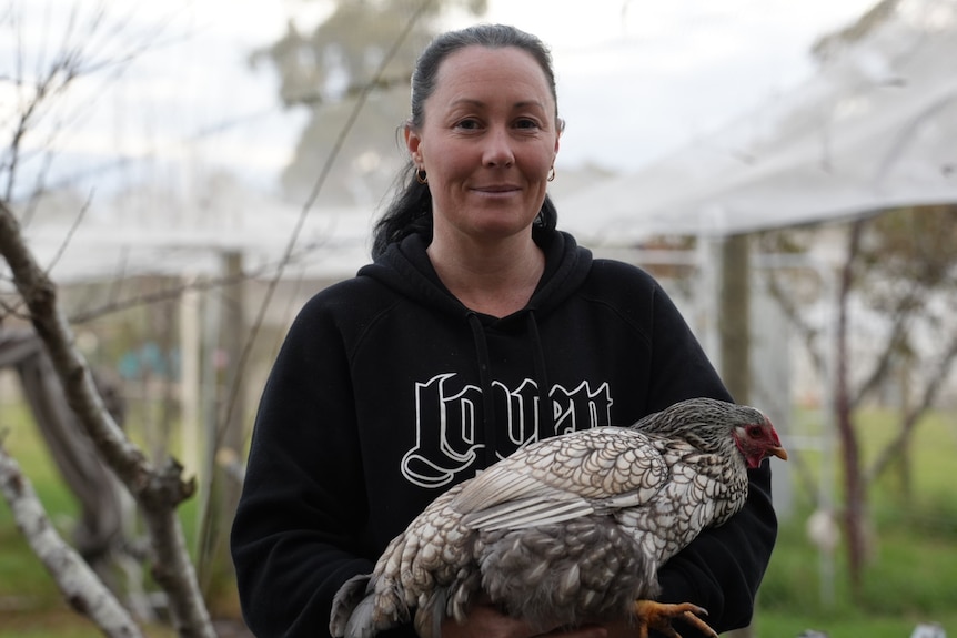 A woman is holding a chicken.