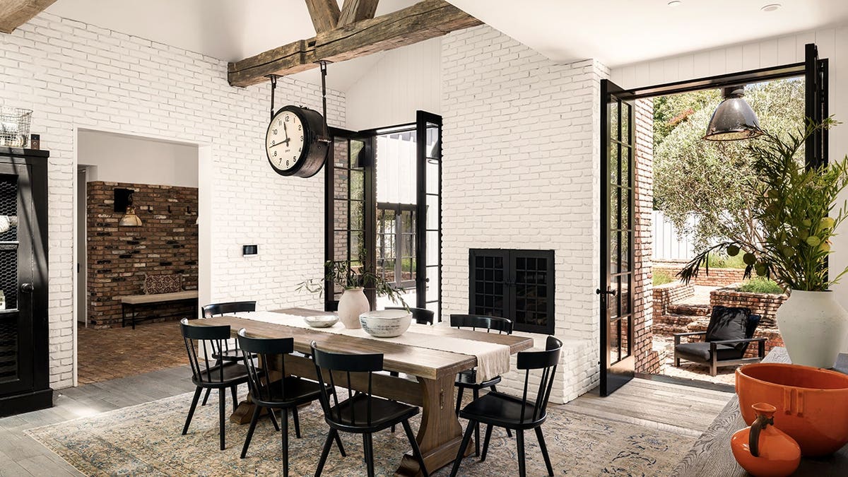 A dining room with a large clock above the table and doors leading outside.