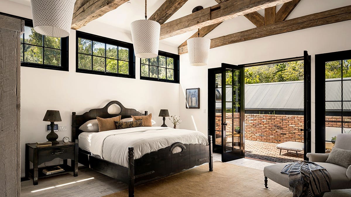 A bedroom with a large bad, beamed ceilings and a private brick balcony.