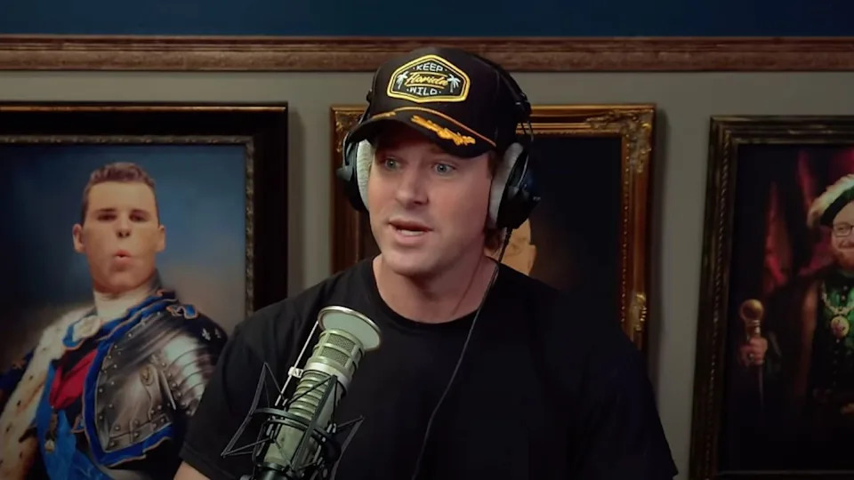 Armie Hammer wearing headphones and a cap sits in front of a microphone, with framed portraits in the background.