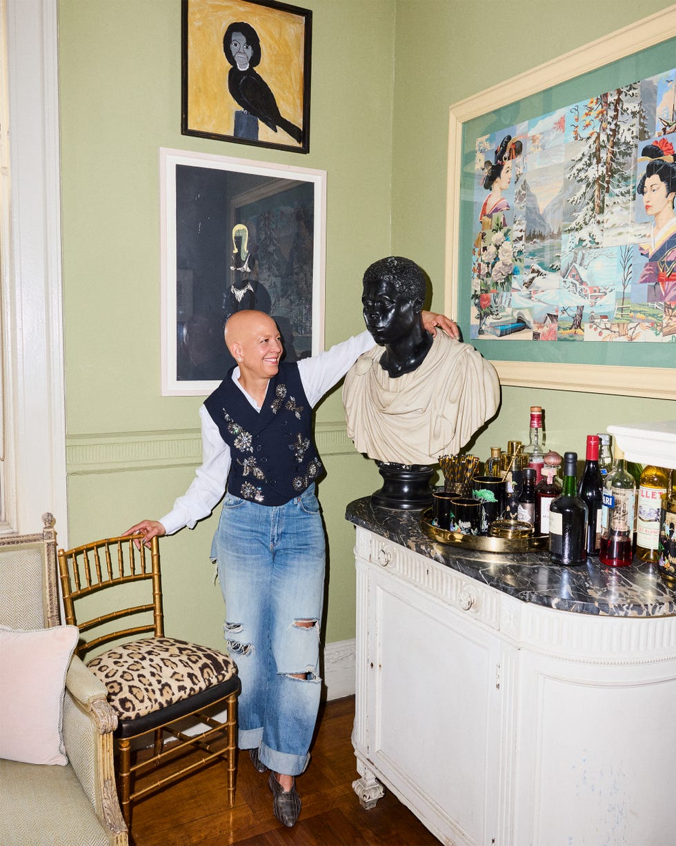 Person smiling next to a black bust in a room with various artworks and a bar setup.