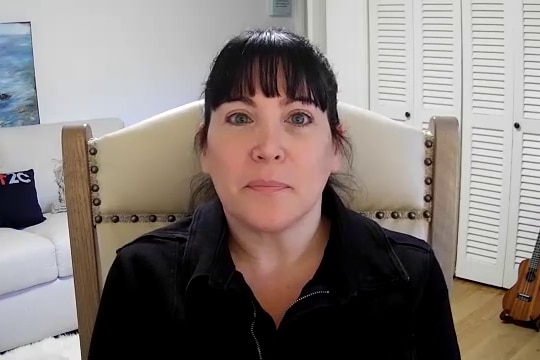 Woman with dark hair wearing a black top sitting in a chair.