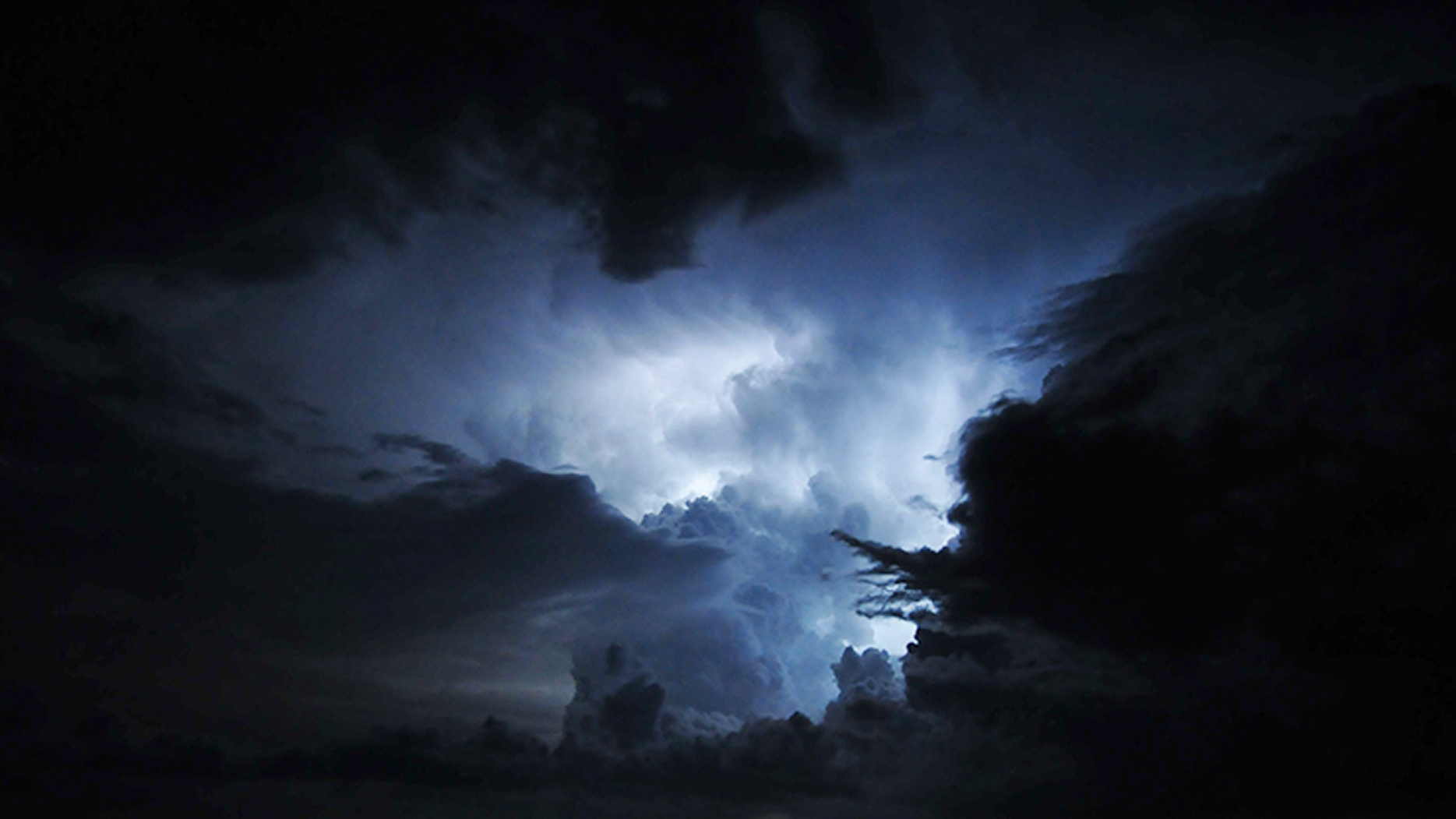 Dark storm clouds illuminated by bright lightning in a night sky