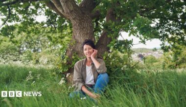 Natalie Fee sits under an oak tree in a grassy meadow