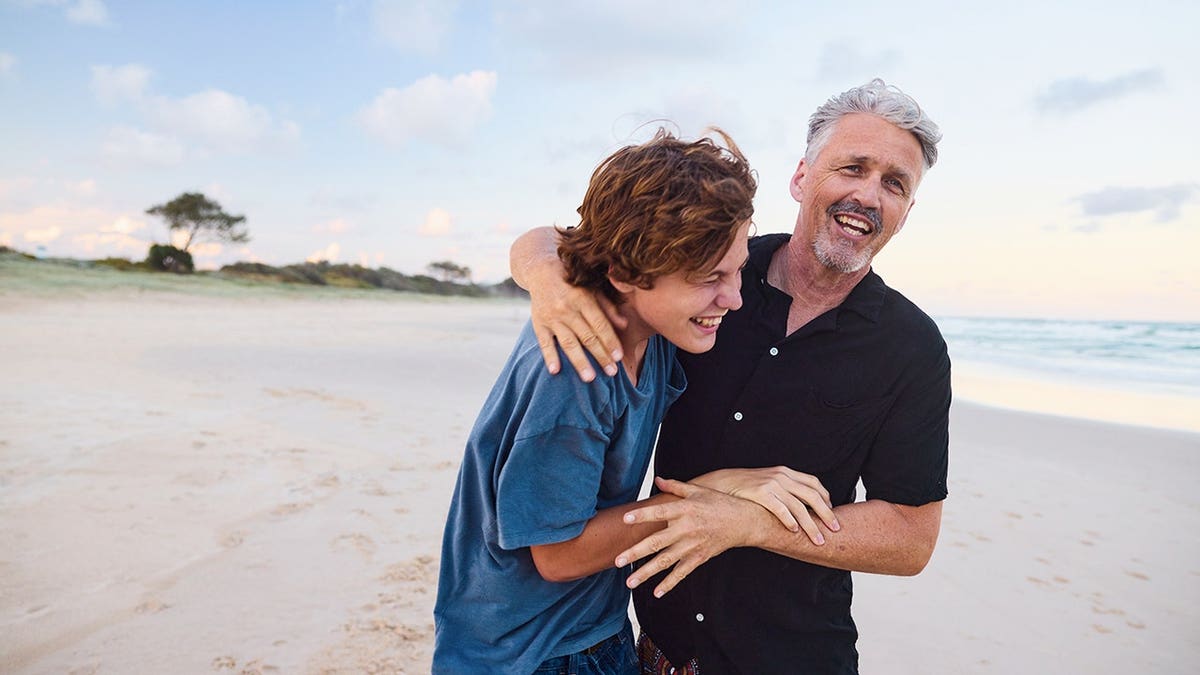 Father and teenage son playing together on a beach in Australia