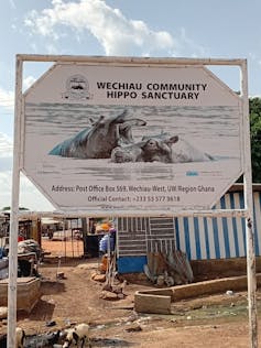 A sign saying Wechiau Community Hippo Sanctuary with houses in the background