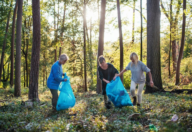 Three older women in a park or forest with blue trash bags
