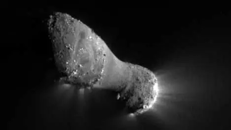 A photo of an oval-shaped comet, with light illuminating it from the back side, which has a sparse trail of dust particles.