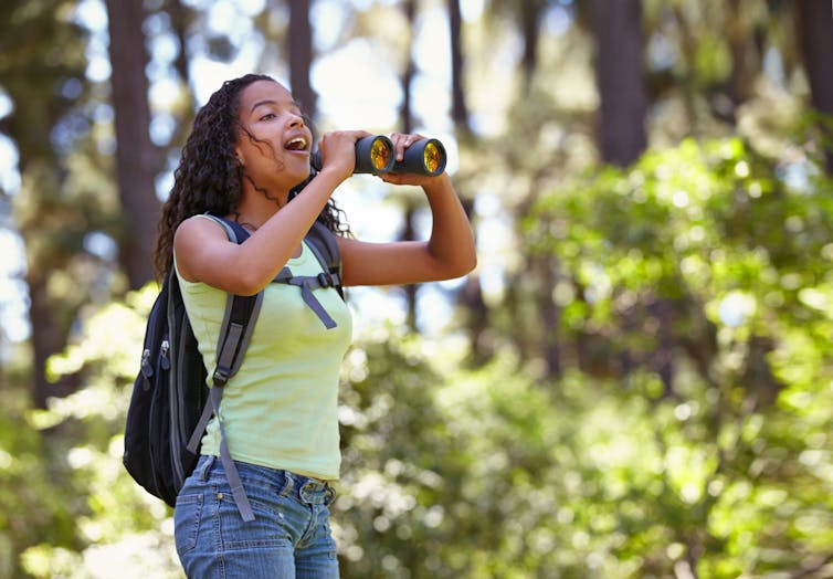 girl in summer clothes, smiling, holding binoculars in woods