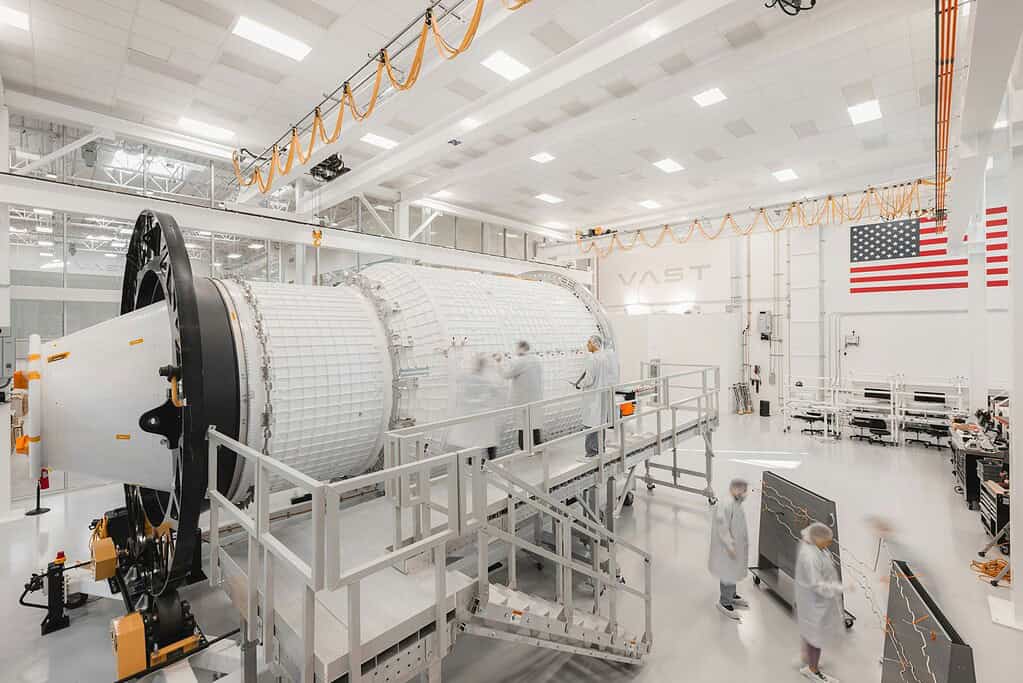 Large spacecraft in a cleanroom with engineers inspecting it.