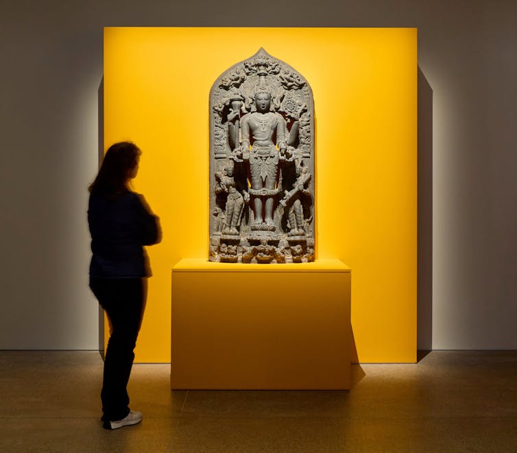 A woman looks upon a large carving of Vishnu.