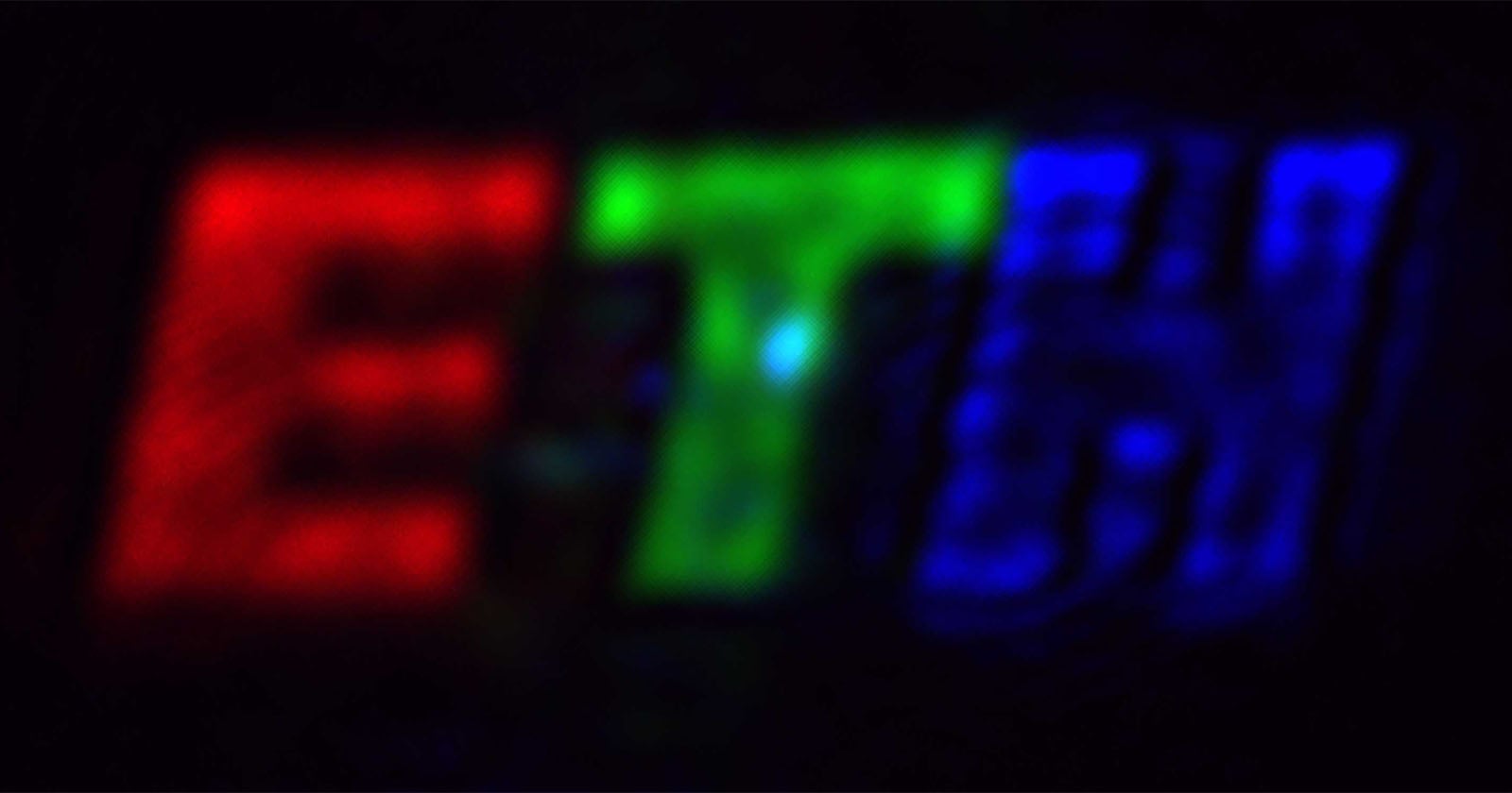 Blurry image showing the letters "ETH" with "E" in red, "T" in green, and "H" in blue, all against a black background.