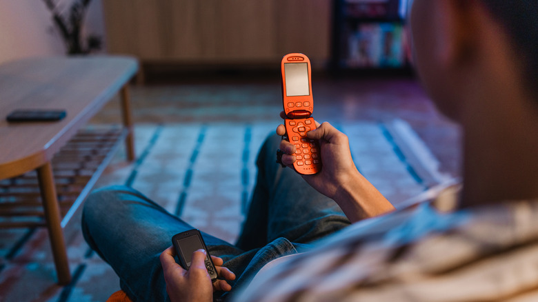 A person sitting and looking at a flip phone