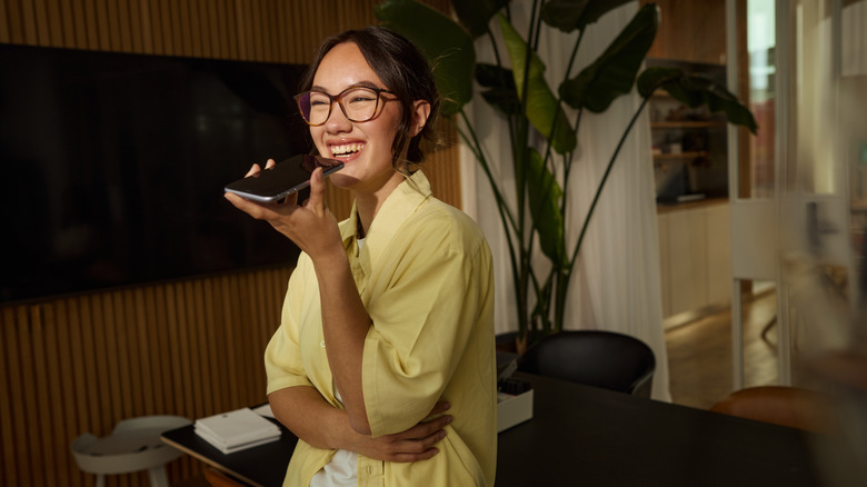 A young person smiling and using a speakerphone