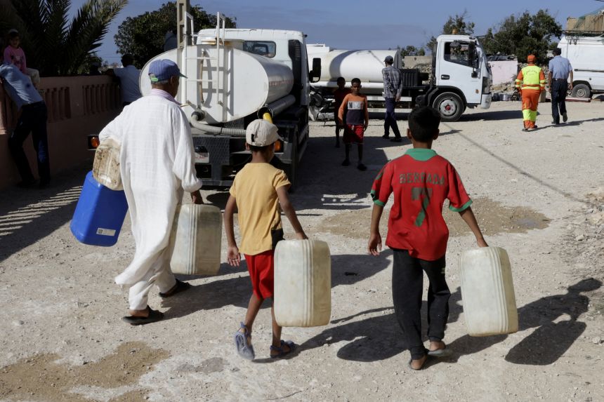 A man and children approach a water tank in the Moroccan village of Sidi Bouchta in August 2024, supplied by a mobile desalination unit — a compact station trucked to communities without reliable water supplies